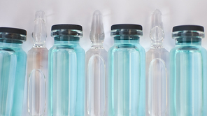 Vial vaccine, top view of glass ampoules with transparent and blue liquid lying on white background, global vaccination concept.