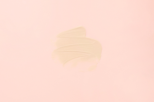 Sample texture of foundation cream for the face close-up. A smear of foundation on a pastel pink background