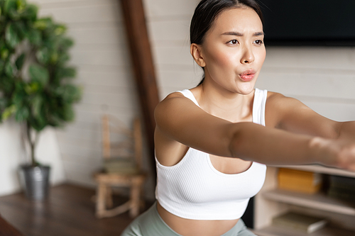 Young asian fitness woman with healthy fit body, doing squats, morning workout, wearing activewear, standing at home in living room and having training session.