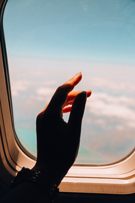 Female hand Airplane flight. View from the window of the plane. Airplane, Aircraft. Vacation travel concept Traveling by air. Airplane Window View Above the Clouds Amazing golden fluffy clouds moving softly on the sky aerial view.