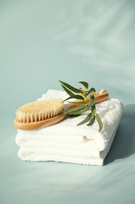 Massage wooden brush on white spa towels with eucalyptus leaves pastel blue background, anti-cellulite massage and body care concept