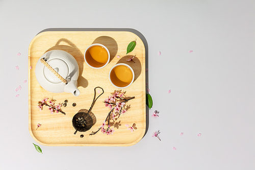 Tea concept, two white cups of tea, teapot, tea strainer and spring sakura branches on concrete background,