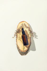 Amber glass bottle on wooden podium, white background, flat lay, top view. Ecological natural cosmetics concept
