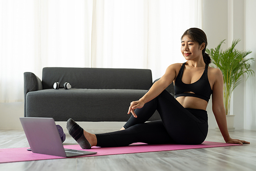 Fit sporty young asian woman online workout exercise at home. Active healthy girl enjoy sport pilates yoga fitness training on laptop computer stretching on yoga mat watching video class.
