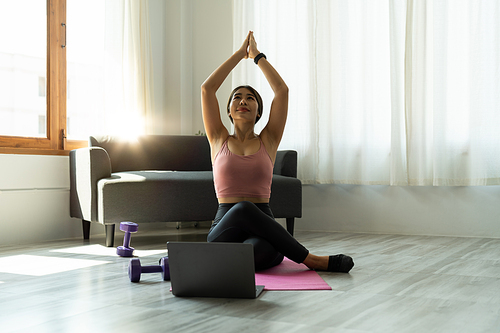 Calm relaxed young asian woman sitting in lotus position with hands up namaste gesture, closed eyes, breathing, resting, deeply meditating, practicing yoga on yoga mat at home.