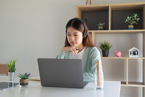 Concentrate asian gial freelancer wearing headset, communicating with client via video computer call. Millennial pleasant professional female tutor giving online language class