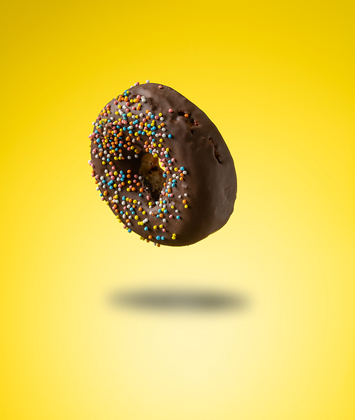 chocolate donuts with multicolored sprinkles levitate on a yellow background