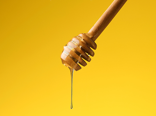 pouring transparent sweet honey from a wooden stick. Yellow background. Food levitates