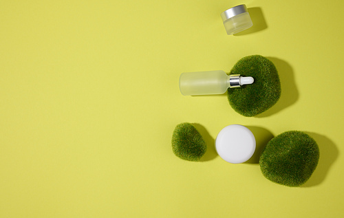 glass cosmetic white bottles with a pipette on a green-yellow background with pieces of moss. Cosmetics SPA branding mockup, top view
