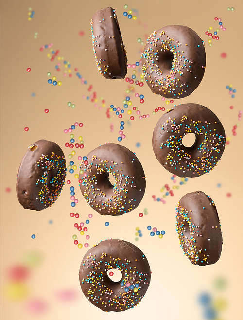 chocolate round donuts with multicolored sugar sprinkles levitate on a beige background