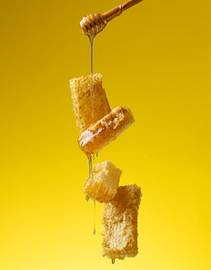pouring transparent sweet honey from a wooden stick on a wax honeycomb. Yellow background