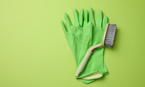 green rubber gloves for cleaning, brushes on a green background, flat lay. Copy space