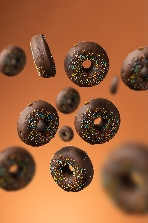 sweet chocolate donuts with multicolored sugar sprinkles on an orange background. Desser in motion and levitation