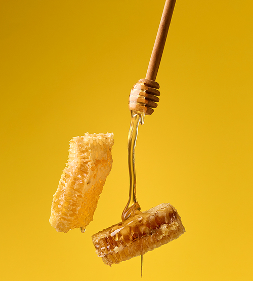 pouring transparent sweet honey from a wooden stick on a wax honeycomb. Yellow background. Food levitates