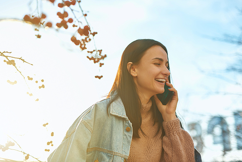 Cheerful female student is glad and joyful calling to someone by her cellphone outdoors