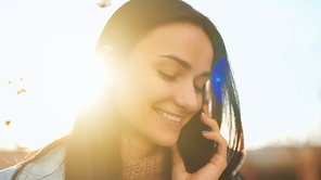 Close up portrait of an adorable young lady taking pleasure from a cheerful phone conversation and sunny autumn evening