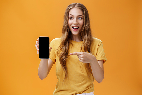 Portrait of excited woman feeling amazed holding awesome new smartphone in hand pointing at cellphone screen popping eyes like crazy at device being charmed with cool technology product.