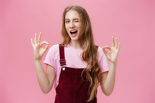 Waist-up shot of assertive good-looking confident teenage girl having everything under control winking delighted and self-assured showing okay gesture confirming job done well over pink background. Copy space