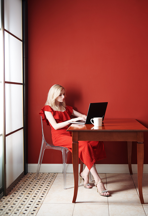 Beautiful young adult woman wearing red jumpsuit and working laptop