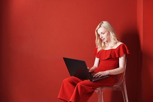 Young adult woman sitting on a chair and working on laptop