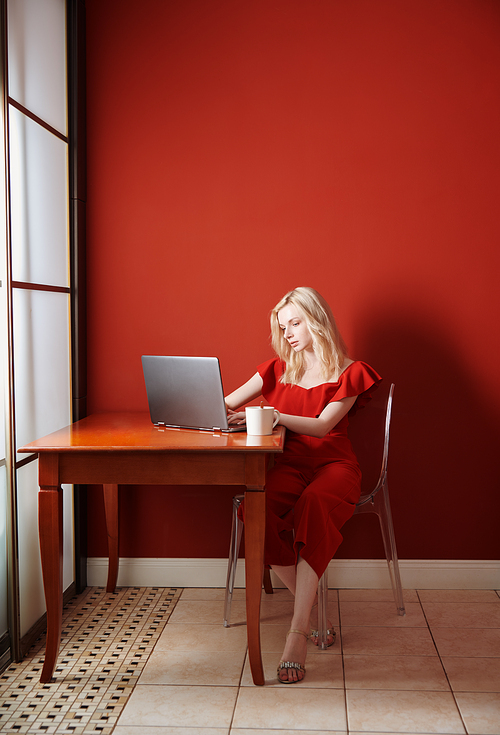 Young adult woman sitting at the table and working on laptop