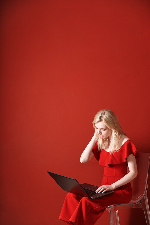 Young adult woman sitting on a chair and working on laptop