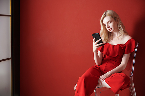 Young adult woman relaxing on a chair and using smartphone