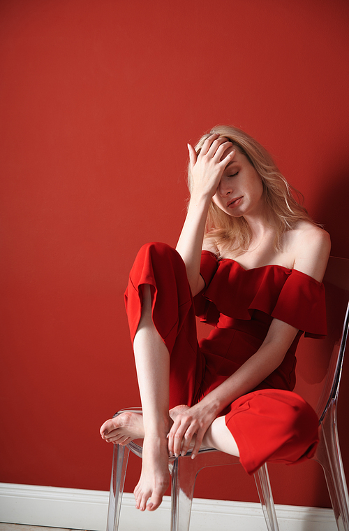 Beautiful young adult woman wearing red jumpsuit relaxing on chair