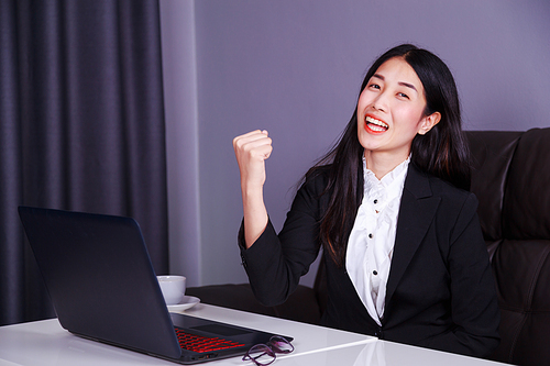 successful young business woman raising arm in happiness with laptop computer