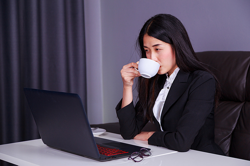 young business woman working on laptop computer and drinking a cup of coffee