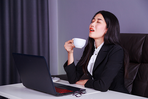 happy young business woman working on laptop computer and drinking a cup of coffee