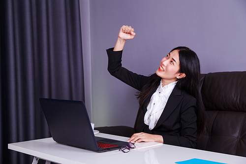 successful young business woman raising arm in happiness with laptop computer