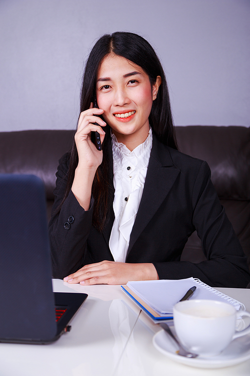 Cheerful young business woman sitting at the desk and talking on mobile phone
