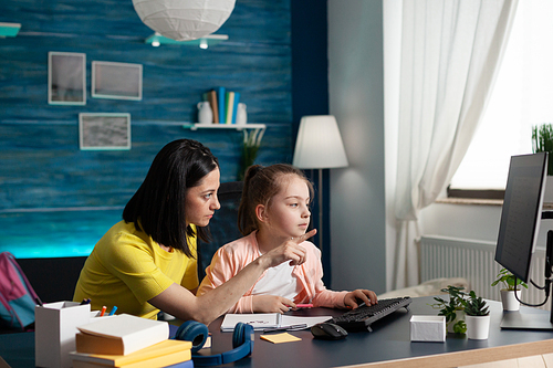 Homeschooled little kid getting assistance from mother with schoolwork and writing essay for online classes. Adult helping pupil girl with lesson, learning knowledge together at home desk