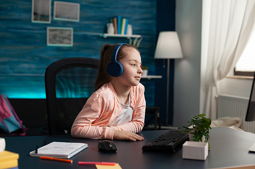 Caucasian student wearing headphones on online class using computer and internet connection at home desk. Smart little child attending elementary school lesson looking at monitor learning