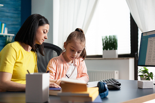 Child and parent doing homework together at home writing exercises for elementary lesson. Caucasian mom helping little girl with educational remote learning system sitting at desk