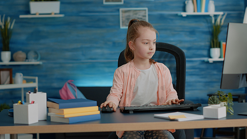 Little girl putting backpack on couch and using computer with keyboard at desk. Young child looking at monitor for homework and school task at home. Schoolgirl with online lessons