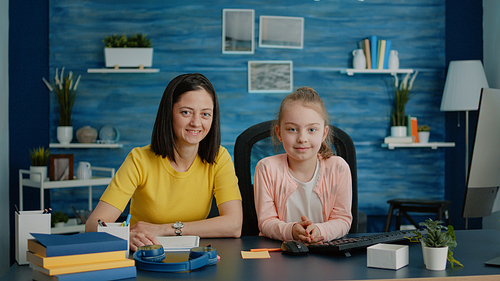 Portrait of mother and child prepared for online classes and homework, sitting at desk. Little girl getting assistance from parent with school work and remote education on internet