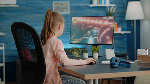 Young child playing action video games on computer at desk. Little girl losing at futuristic shooting game on monitor. Player gaming for fun and entertainment after online classes