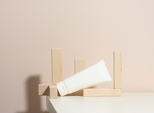 empty white plastic tubes for cosmetics on a beige background with wooden blocks. Packaging for cream, gel, serum, advertising and product promotion, mock up