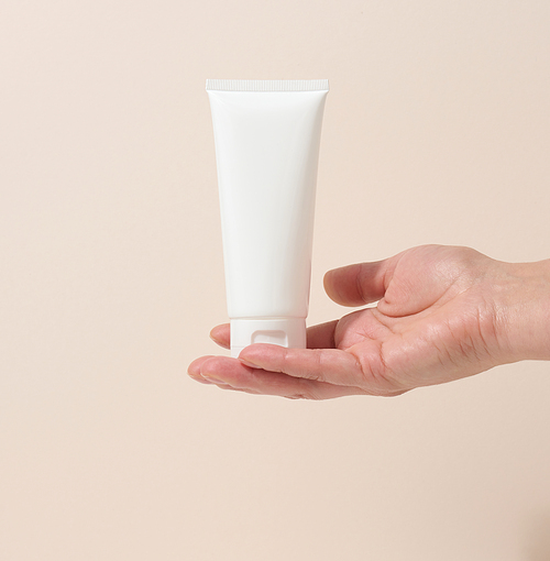 female hand holds empty white plastic tubes for cosmetics. Packaging for cream, gel, serum, advertising and product promotion, mock up