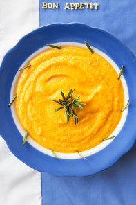 pumpkin soup in a blue plate with rosemary on a napkin with flowers, lettering bon appetit