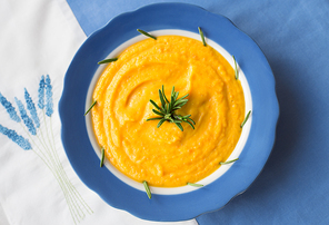 pumpkin soup in a blue plate with rosemary on a napkin with flowers