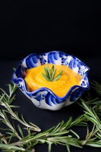 pumpkin soup in a blue plate on a black background with a branch of rosemary