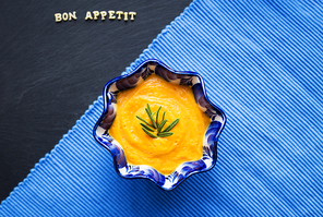 pumpkin soup in a blue plate on a black background with a blue cloth, close-up