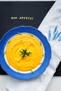 pumpkin soup in a blue plate on a black background with a white cloth, close-up