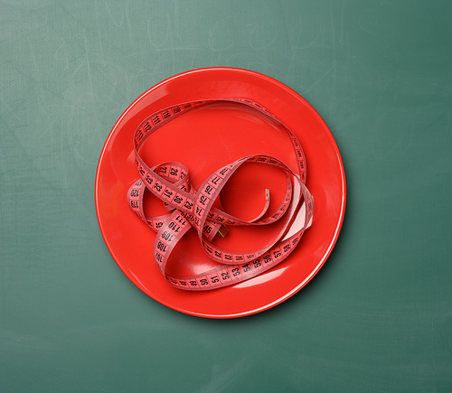 red round plate and red measuring tape on a green background, weight loss concept, flat lay