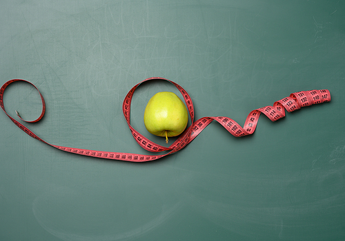 ripe apple wrapped with a centimeter on a green background, body weight control concept, weight loss