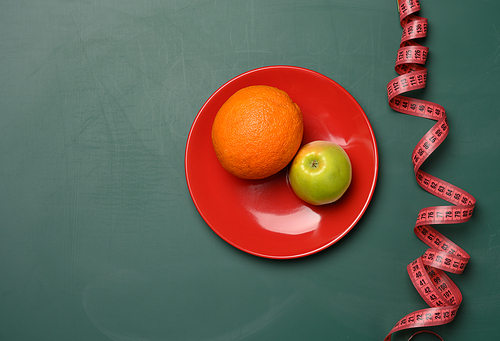 green apple and red round plate, red measuring tape on a green background, weight loss concept, flat lay