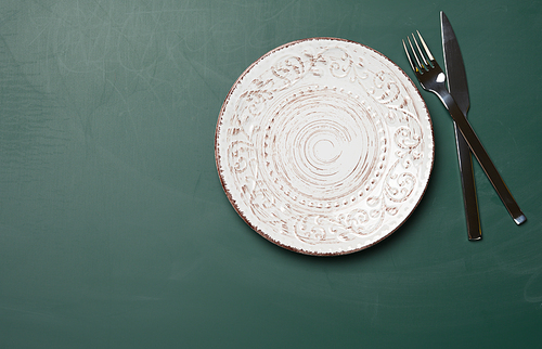 empty white round ceramic plates, fork with knife on a green background, top view. Table setting